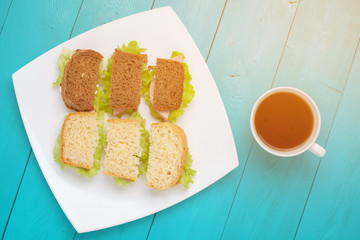 Bruschetta of white and black bread lay on a plate. The dish of sandwiches standing on the wooden surface. A Cup of tea next to a plate of sandwiches. Flat lay of food on a table lit by the bright sun