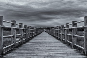 Obraz premium Black and white of a couple walking away on a pier as a storm is rolling in