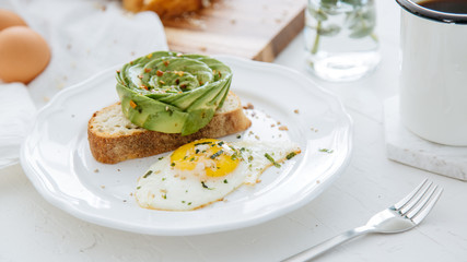 Breakfast setting featuring avocado rose on toast, sunny side up egg and coffee.