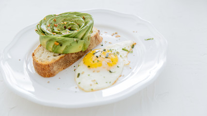 Avocado rose on toast with sunny side up egg on white plate and white background.