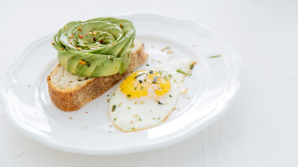 Avocado rose on toast with sunny side up egg on white plate and white background.