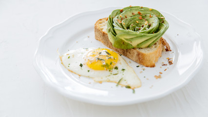 Avocado rose on toast with sunny side up egg on white plate and white background.