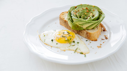 Avocado rose on toast with sunny side up egg on white plate and white background.