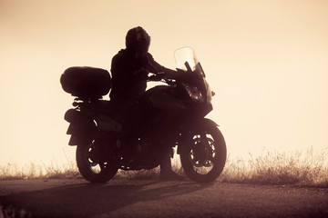 silhouette of a man riding a motorbike on foggy road in early morning