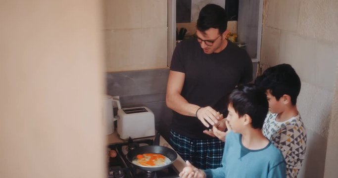 Father and sons cooking eggs for breakfast in the morning