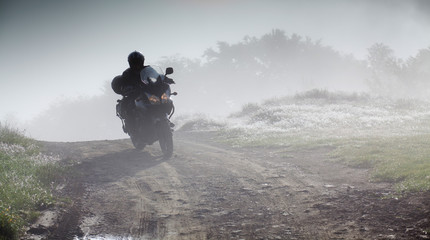 silhouette of a man riding a motorbike on foggy road in early morning