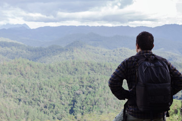 young man whit backpack on top of the mountain looking to the forest