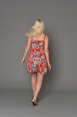 full length portrait of blonde girl wearing red floral dress, standing pose on grey studio background.