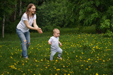 Fototapeta premium Family. Mom and son are walking around meadow holding hands. Pregnant girl is happy. Little boy learn to walk. Yellow dandelions grow in meadow.