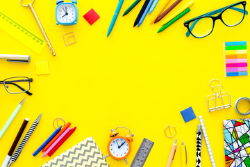 Education background, frame. School, student, office supplies. Stationery, glasses, alarm clock, notebook on yellow background top view copy space