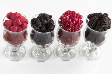 Raspberry, a big black blackberry, red currant and mulberry are located in clear glass on a light background