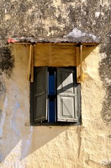 Rustic stone dwelling with wooden window shutters and a corrugated iron portico