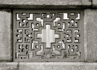 Black and white image of a window opening with an ornate stone patterned grill in a geometric...