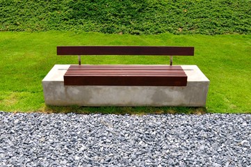 Modern concrete park bench with wooden slatted seats in front of a loose pebbled footpath