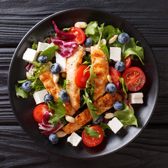 Dietary snack salad with blueberries, feta, chicken, nuts, tomatoes and lettuce close-up. top view...