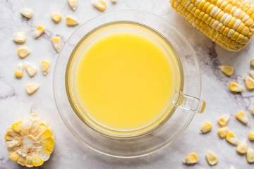 A cup of corn milk and fresh sweet corn on marble table. Top view