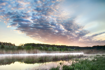 Sunrise on a summer morning, colorful clouds in the sky. The fog is mistaken over the river. Nature