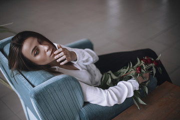A beautiful girl is sitting on a blue velvet chair and is resting. A woman in black trousers and a...
