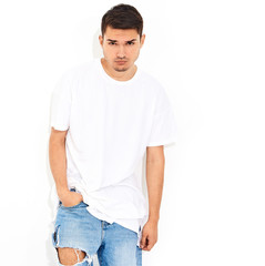Obraz premium Portrait of handsome young model man dressed in jeans clothes and T-shirt posing on white background. Crossed arms