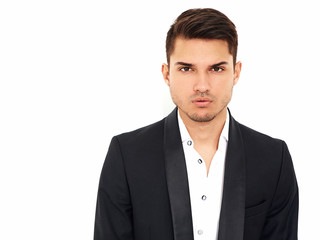 portrait of handsome fashion stylish hipster lumbersexual businessman model dressed in elegant black classic suit posing near white wall in studio. Metrosexual