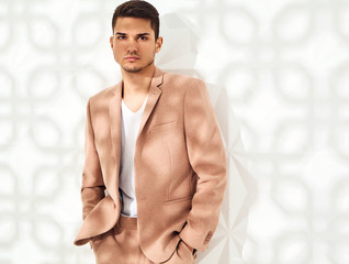 Fototapeta na wymiar Fashion stylish lumbersexual model dressed in elegant light pink suit posing near white wall in studio. Metrosexual