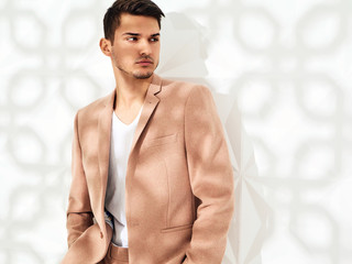 Fashion stylish lumbersexual model dressed in elegant light pink suit posing near white wall in...