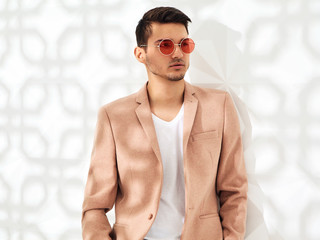 Fashion stylish lumbersexual model dressed in elegant light pink suit posing near white wall in...