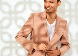 Fashion stylish lumbersexual model dressed in elegant light pink suit posing near white wall in...