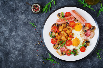 English breakfast - fried egg, beans, tomatoes, mushrooms, bacon and sausage. Tasty food.  Top view. Flat lay.