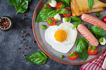 Breakfast on Valentine's Day - fried eggs in the shape heart, sausage, toast and caprese salad of a tomato, basil and mozzarella.  Homemade, tasty food. Top view. Flat lay