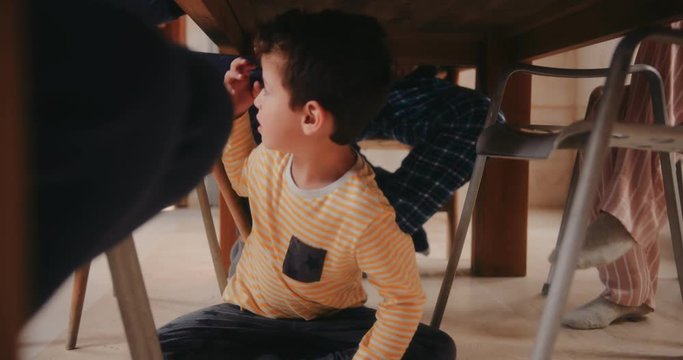 Sad crying boy sitting under kitchen table during breakfast
