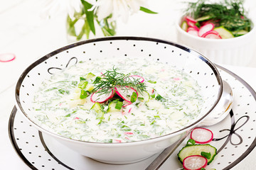 Cold soup with fresh cucumbers, radishes with yoghurt in bowl on wooden background. Traditional russian food - okroshka. Vegetarian meal.