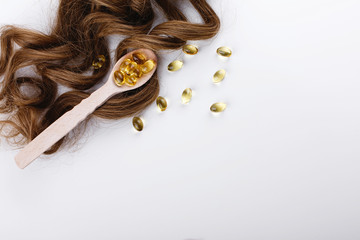 Oil capsule for hair with vitamin E lie on wooden spoon on brown hair curls