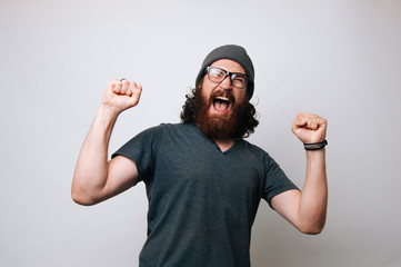 Fototapeta premium Lucky young bearded hipster man over grey background. Man with glasses acts like he won something