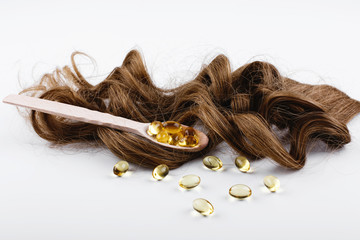 Oil capsule for hair with vitamin E lie on wooden spoon on brown hair curls