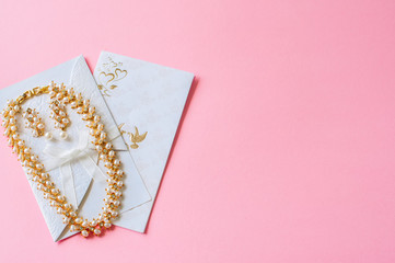 Wedding concept. Invitation cards and pearl necklace and earrings on a pink background.