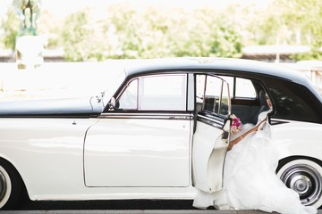 Look from the outside at a bride sitting inside a white retro car
