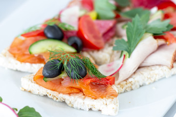 Sandwich with smoked salmon served on a rice waffle decorated with olive, cucumber, paprika and a sprig of fennel on a white plate closeup