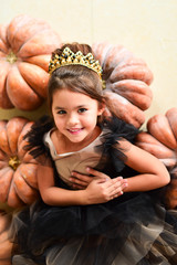 Beautiful little girl in black evening gawn sits on the pampkins in a studio