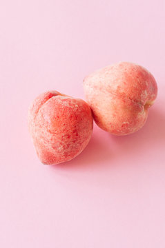 Two fresh ripe peaches on a pink background.