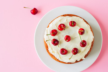 Homemade pound cake with cream cheese frosting decorated with fresh ripe cherries on a light pink background. Overhead view.