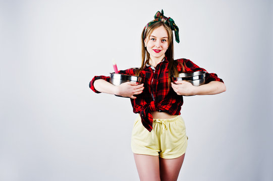 Young funny housewife in checkered shirt and yellow shorts pin up style with two saucepan isolated on white background.