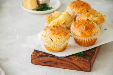 Savory double cheese muffins on a wooden board. White stone background.