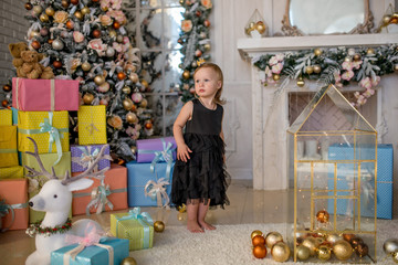 Little girl in black dress sits among Christmas decorations