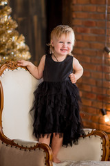 Little girl in black dress sits among Christmas decorations