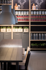 Working wooden table desk with modern lamps overhead and decoration shelves in the background. Coworking space or design office workspace concept.