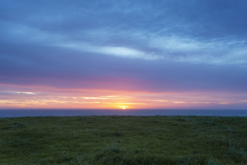 Fototapeta na wymiar Sunrise Over Green Hill and Ocean