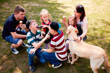 The children and parents eatting ice creams and sitting near dog