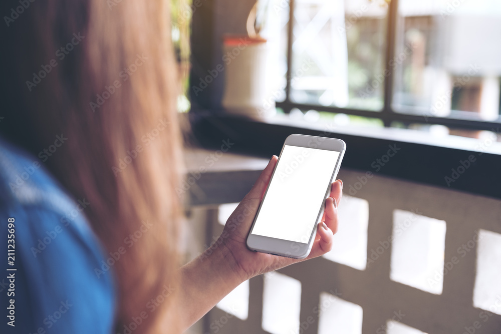 Wall mural mockup image of a woman holding white mobile phone with blank desktop screen in cafe