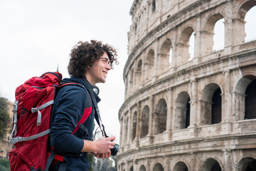 Fototapeta na wymiar Handsome young tourist man with a camera and backpack taking pictures of Colosseum in Rome, Italy. Young tourist taking pictures of Colosseum